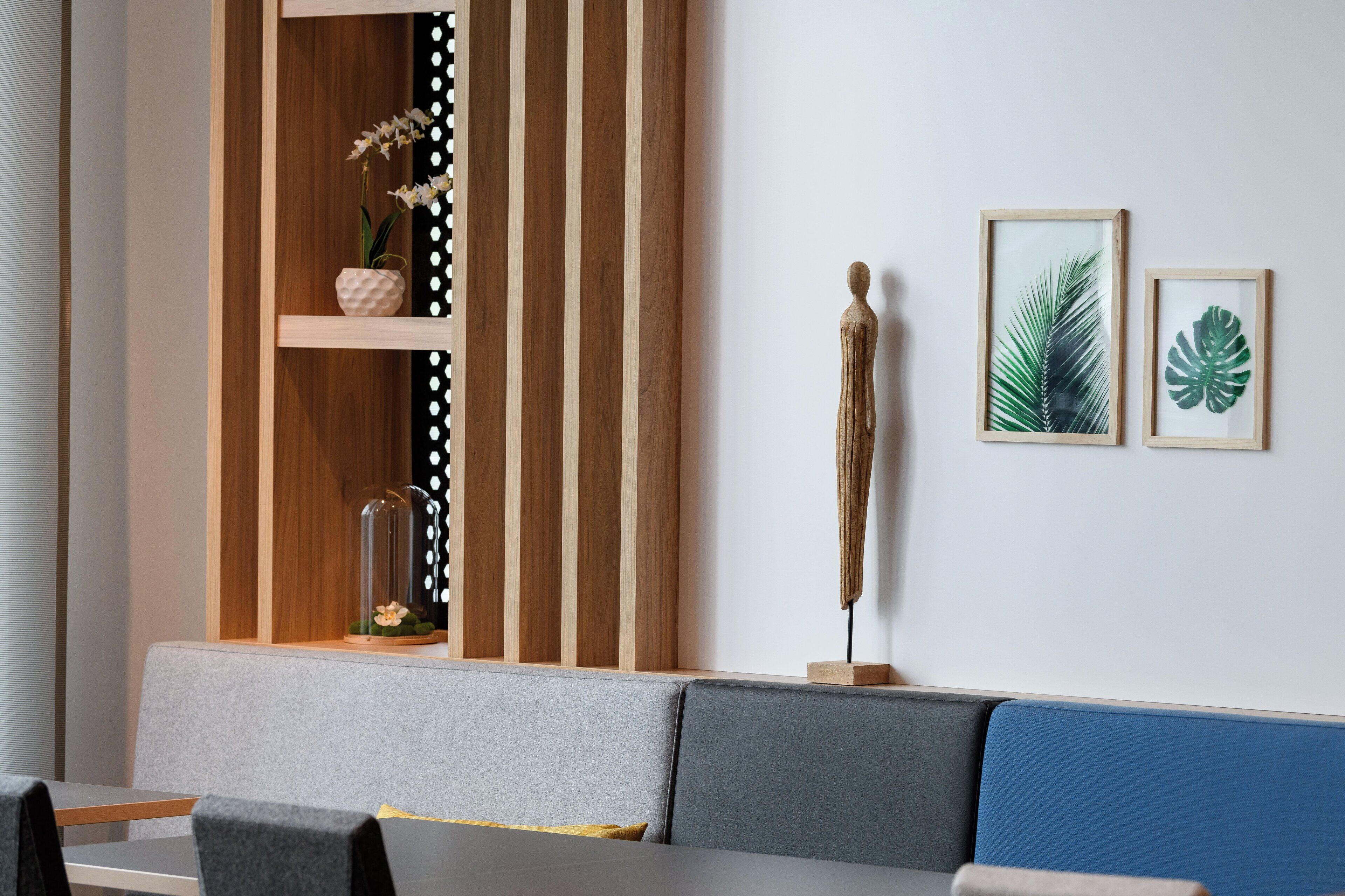 A modern interior with a wooden panel wall, a seating area with grey and blue cushions, and framed botanical prints on the wall.