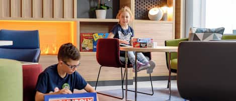 Una sala de estar moderna con un sofá, sillas y una mesa donde dos niños juegan al Monopoly.