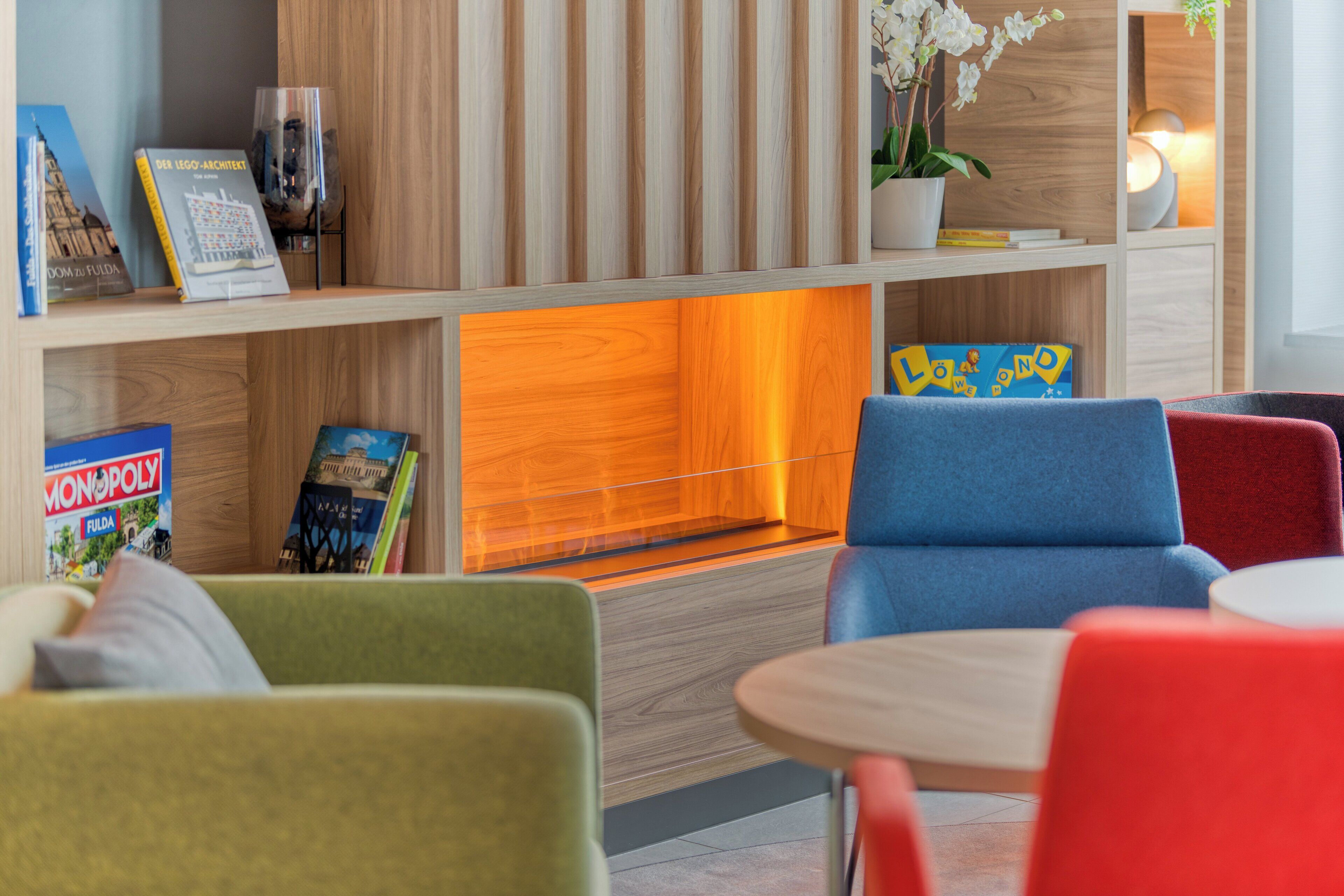 A modern living room with a fireplace, colorful chairs, and bookshelves.
