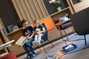 A modern room with a wooden panel wall, a bookshelf with books and a board game, and a red chair.
