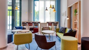 A modern lounge area with round tables and colorful chairs, large windows with natural light, and a mix of wooden and metal decor. - Holiday Inn Express Fulda by IHG (Fulda)