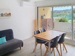 Una sala de estar moderna con un sofá, una mesa de comedor con sillas, un ventanal con vistas a zonas verdes y colinas, y un equipo de aire acondicionado en la pared.