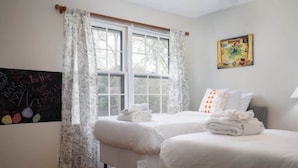 A bedroom with two beds, a window with curtains, a wall-mounted painting, and a chalkboard with writing. - Pet Friendly & Fast WiFi - Fresh at Forest Hills (Montgomery)