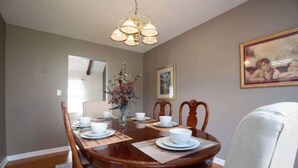 A dining room with a wooden table set for four, chairs, a chandelier, a vase with flowers, and framed pictures on the wall. - Pet Friendly & Fast WiFi - Fresh at Forest Hills (Montgomery)