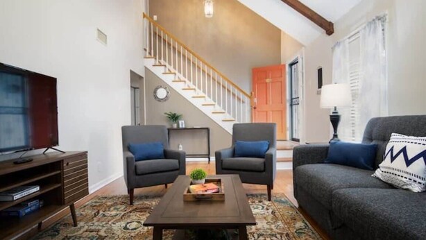 A living room with a sofa, two armchairs, a coffee table, a TV, and a staircase leading to another room. - Pet Friendly & Fast WiFi - Fresh at Forest Hills (Montgomery)