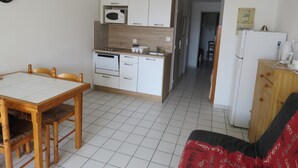 A compact kitchen with white cabinets, a microwave, and a dishwasher. There is a dining table with chairs and a small wooden cabinet with a microwave on top.