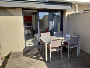 Un patio al aire libre con una mesa y sillas, una puerta corrediza de vidrio que da a una cocina y una pared blanca.