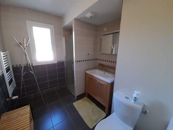 Un baño con ducha, inodoro, lavamanos y ventana.
