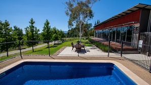 A swimming pool with a patio area, surrounded by a fence and trees.