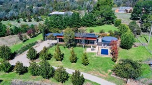 An aerial view of a modern house with a large backyard, solar panels, and a swimming pool.