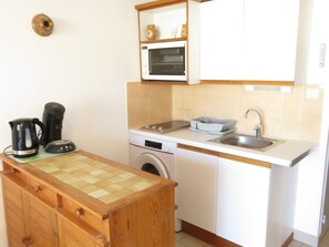 A compact kitchen with a washing machine, a coffee maker, a microwave, and a sink.