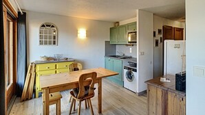 A compact kitchen with a wooden table and chairs, a washing machine, and a refrigerator. - Modern 2-Bedroom Apartment + Cabin, Close to Combloux Center (Combloux)
