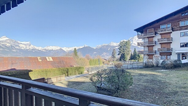 A balcony with a view of a mountain range, a building with balconies, and a fenced area with shrubs. - Modern 2-Bedroom Apartment + Cabin, Close to Combloux Center (Combloux)