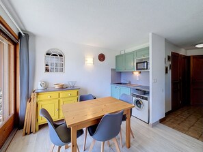 A compact kitchen with a dining area, including a wooden table and chairs, a washing machine, and a microwave. - Modern 2-Bedroom Apartment + Cabin, Close to Combloux Center (Combloux)