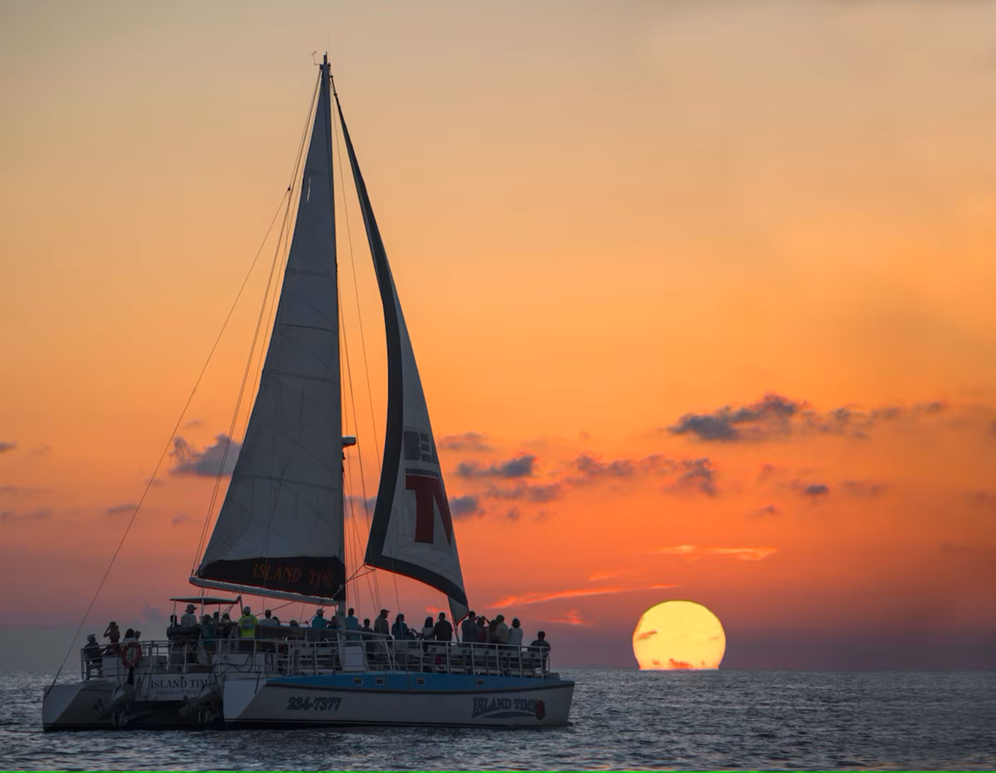 Veleiro com passageiros ao pôr do sol.