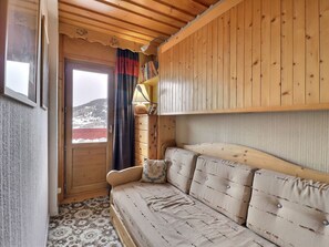 A cozy room with a wooden ceiling, a sofa with a patterned cushion, a lamp, and a view of a snowy landscape through a window.