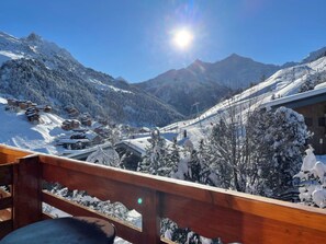 A snow-covered mountain landscape with a wooden balcony overlooking a ski resort.