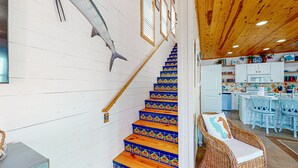 A staircase with colorful tiles, a wooden ceiling, and a kitchen area with white cabinets and blue chairs. - Pet Friendly, 2 Shared Heated Pools, Parking for 3, Gated in Village Walk (Port Aransas)