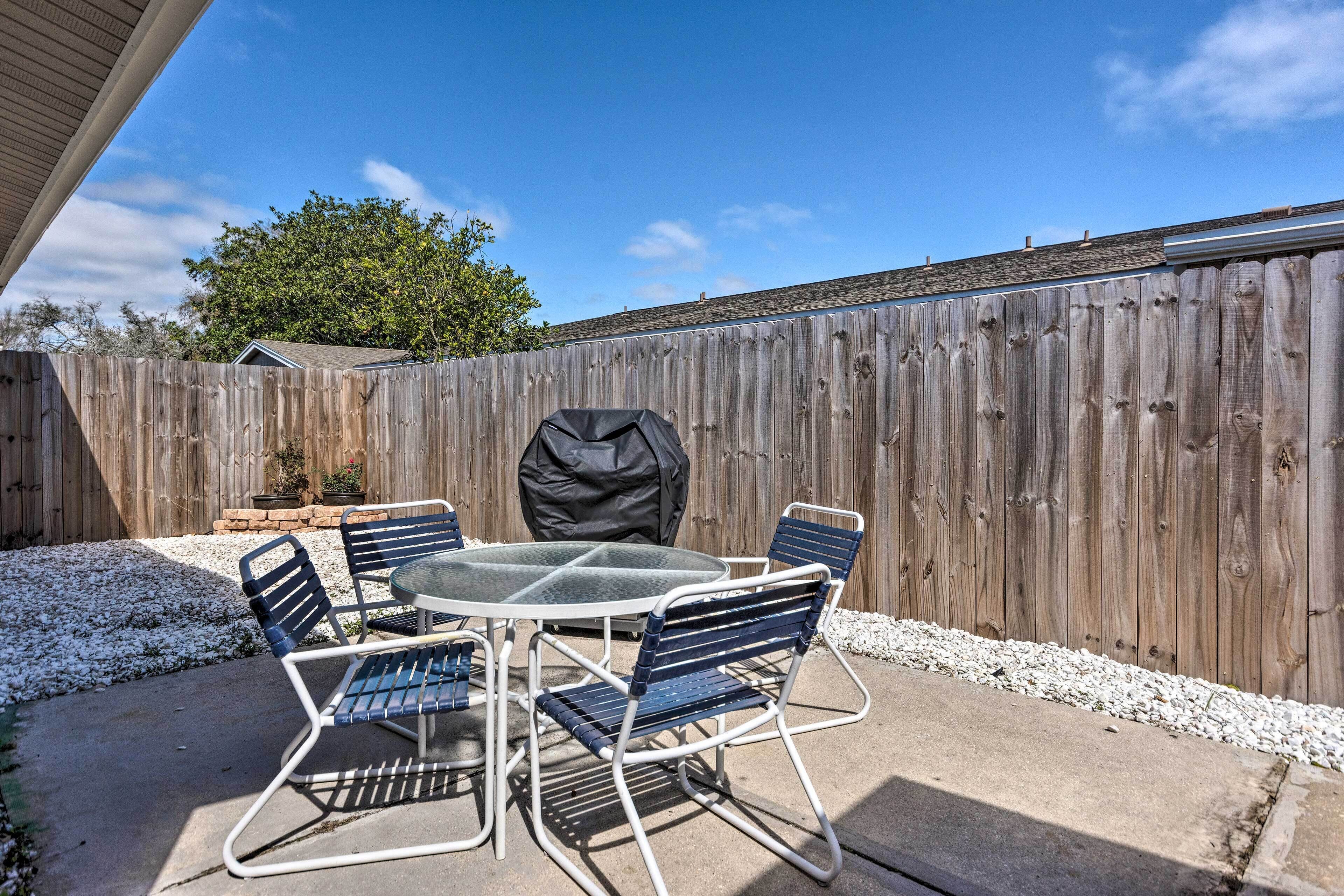 Een terras met een ronde tafel en vier stoelen, een barbecue en een houten omheining op de achtergrond.