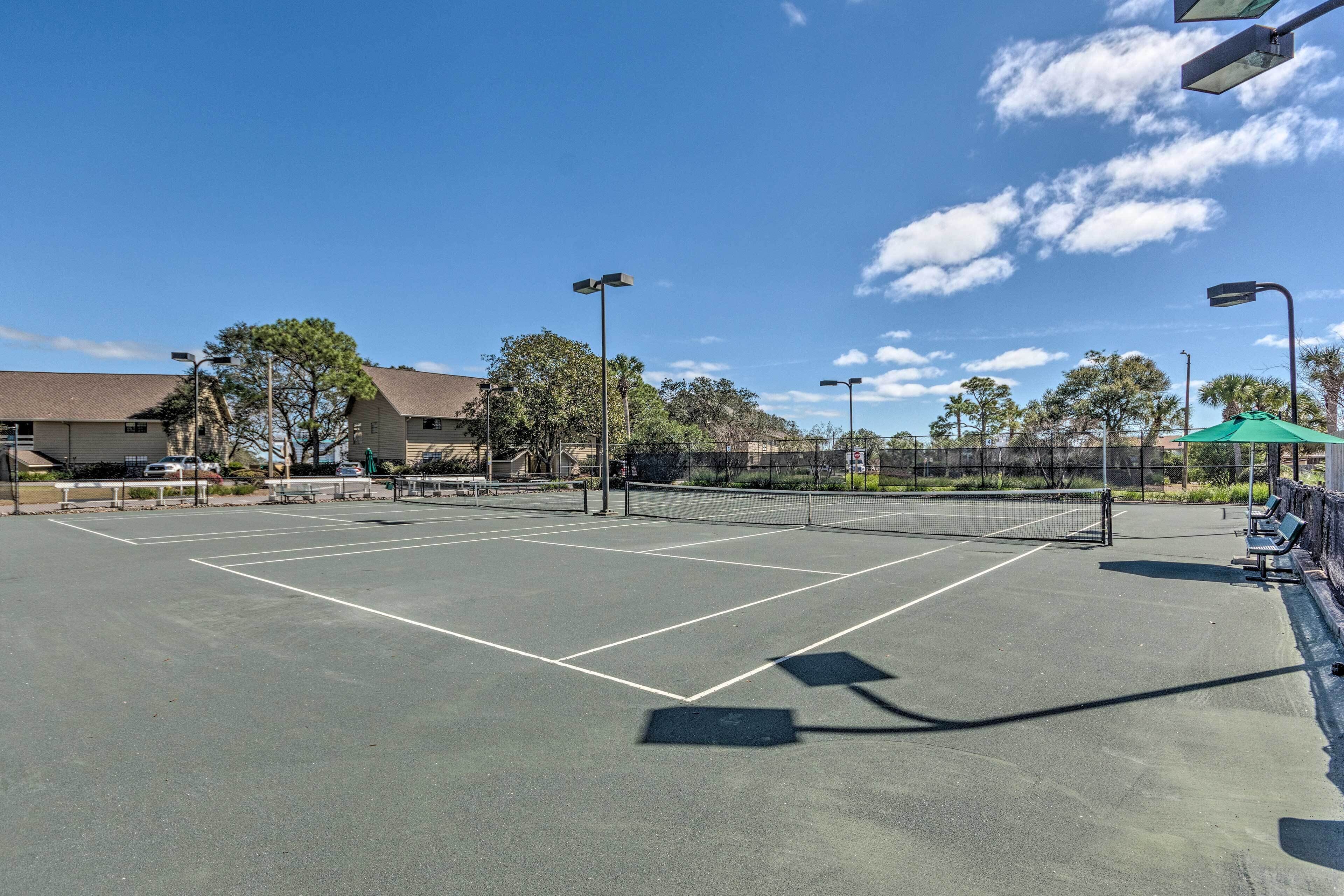 Un court de tennis en plein air, doté d’un filet, entouré d’arbres et de bancs.