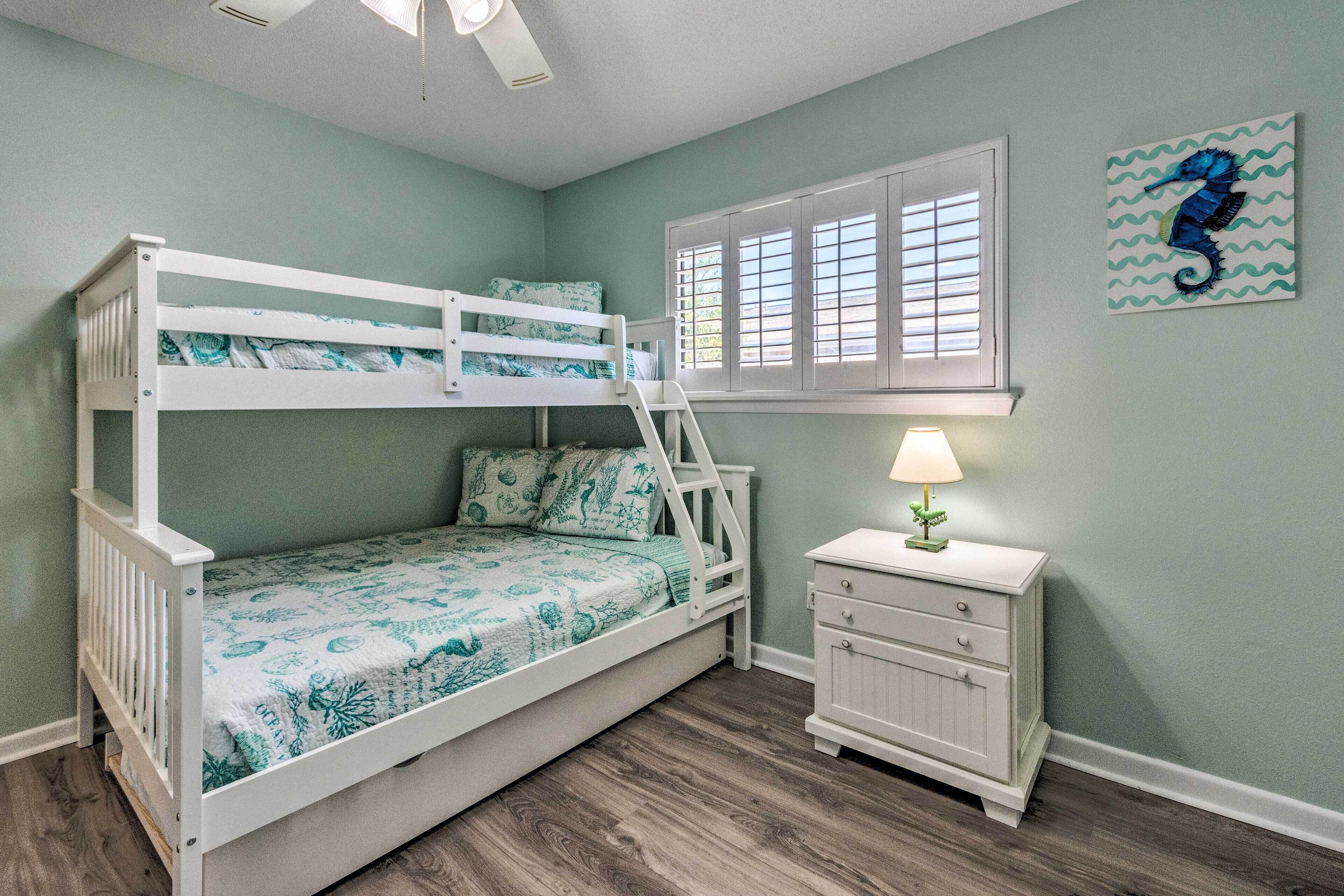 A bunk bed with a ladder, a nightstand with a lamp, and a window with shutters.