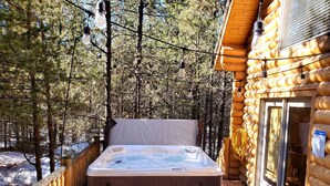 A hot tub on a wooden deck with a view of a forest.