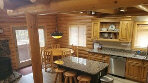 A log cabin interior with a kitchen, dining area, and a stone fireplace.
