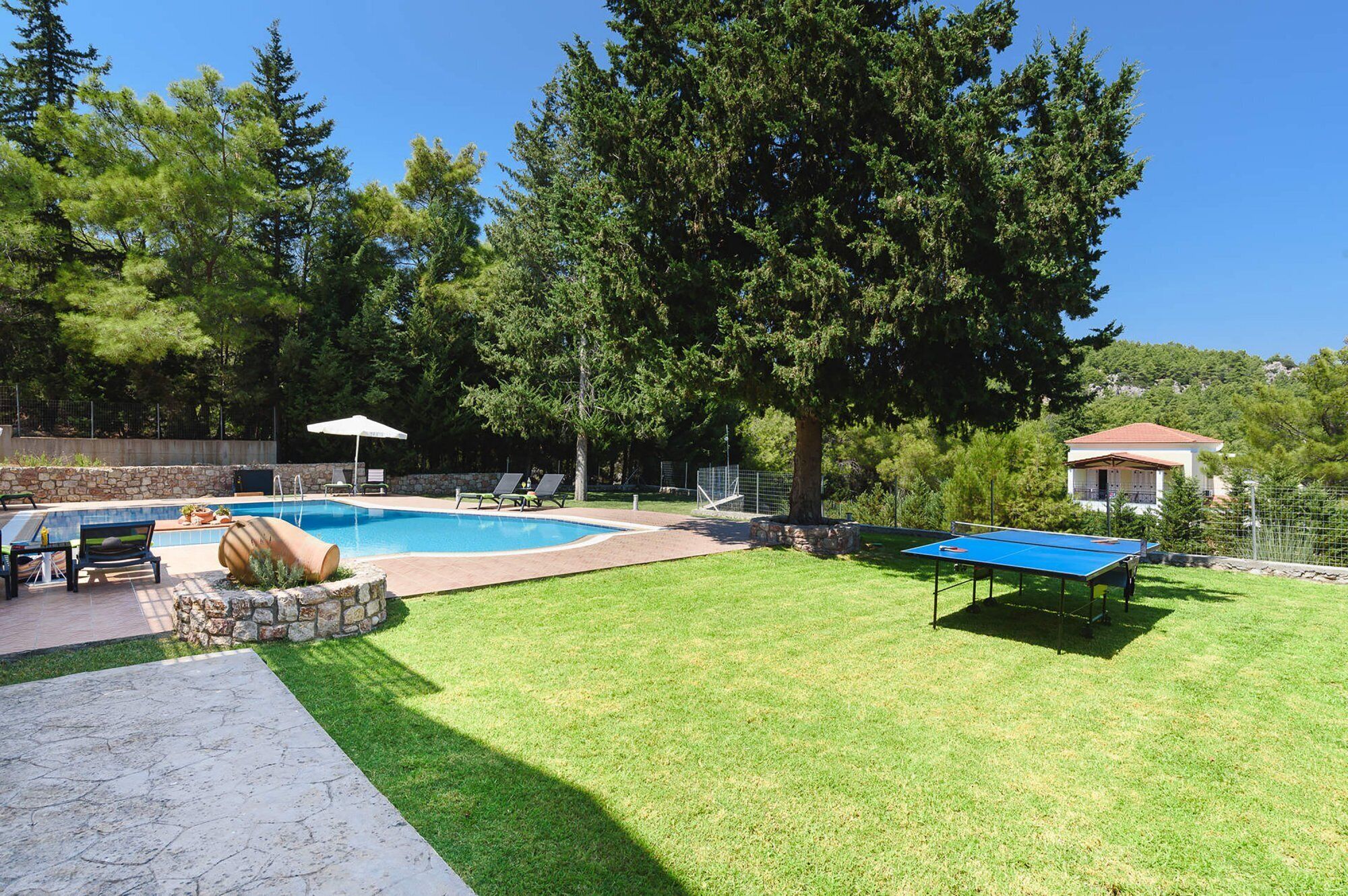 Una piscina, sillas de descanso, mesa de ping pong y un muro de piedra.