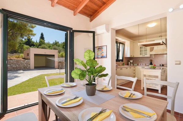 A dining area with a table set for four, a potted plant, and a view of the outside.