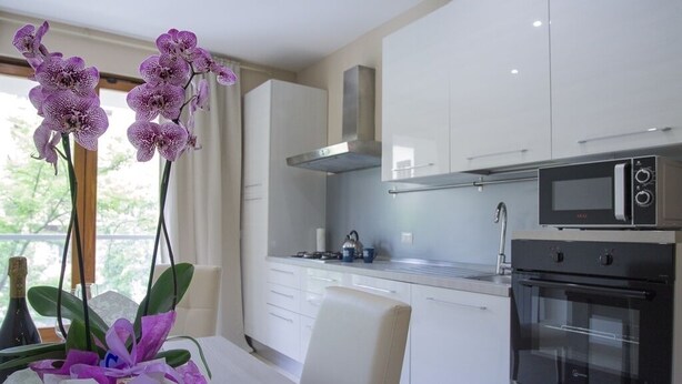 A modern kitchen with white cabinets, a stainless steel range hood, a microwave, and an oven. - Appartamento con Camera da Letto e Balcone (Catania)