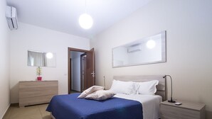 A bedroom with a bed, bedside tables, a dresser, a mirror, and an air conditioning unit. - Appartamento con Camera da Letto e Balcone (Catania)