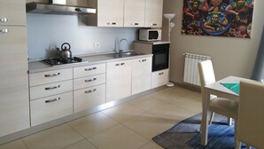 A modern kitchen with white cabinets, a gas stove, a microwave, and a small oven. There is a dining table with a chair and a colorful painting on the wall. - Appartamento con Camera da Letto e Balcone (Catania)
