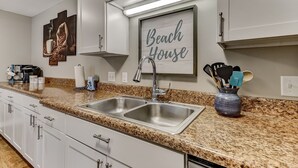 A kitchen with white cabinets, a granite countertop, a double sink, and a framed sign that reads "Beach House". - Pet Friendly | Updated Forest Ridge Villa | Short Walk to the Beach | Community Pool & Tennis (Fernandina Beach)