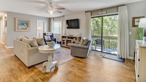 A spacious living room with a ceiling fan, a fireplace, a television, and a balcony with curtains. - Pet Friendly | Updated Forest Ridge Villa | Short Walk to the Beach | Community Pool & Tennis (Fernandina Beach)