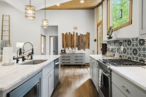 A modern kitchen with a central island, wooden flooring, and pendant lighting.