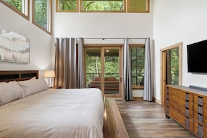 A bedroom with a bed, a TV, a wooden dresser, and a sliding glass door leading to a balcony.