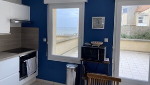 A compact kitchen with a view of the sea, a microwave, and a small shelf with a bowl.