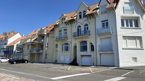 A row of multi-story buildings with balconies, a parking lot, and a clear blue sky.
