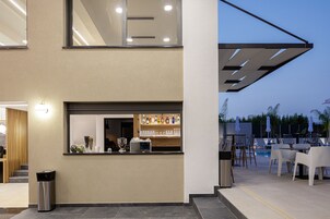 Un bar moderno con barra, estantes llenos de botellas y un área de estar junto a la piscina con sombrillas.