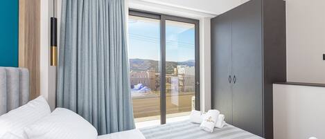A hotel room with a large bed, a wardrobe, and a view of the city through a large window.