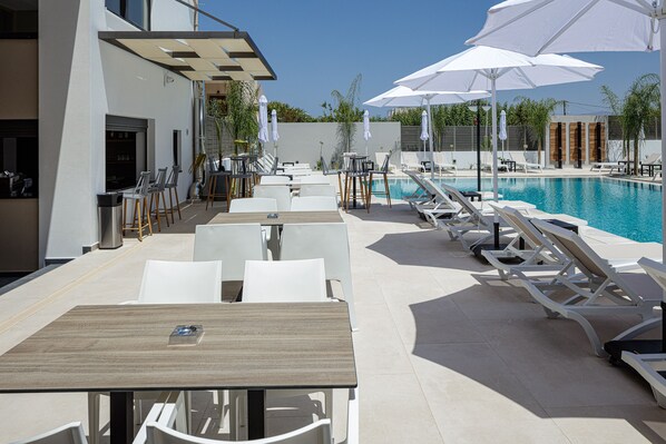 Un área junto a la piscina con sillones de descanso y sombrillas, piscina y zona de comedor con mesas y sillas.