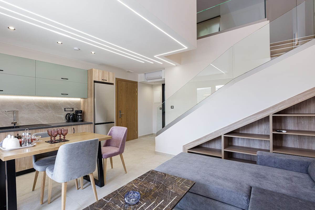 A modern kitchen with a dining area, a staircase, and a living room with a sofa.