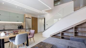 A modern kitchen with a dining area, a staircase, and a living room with a sofa.
