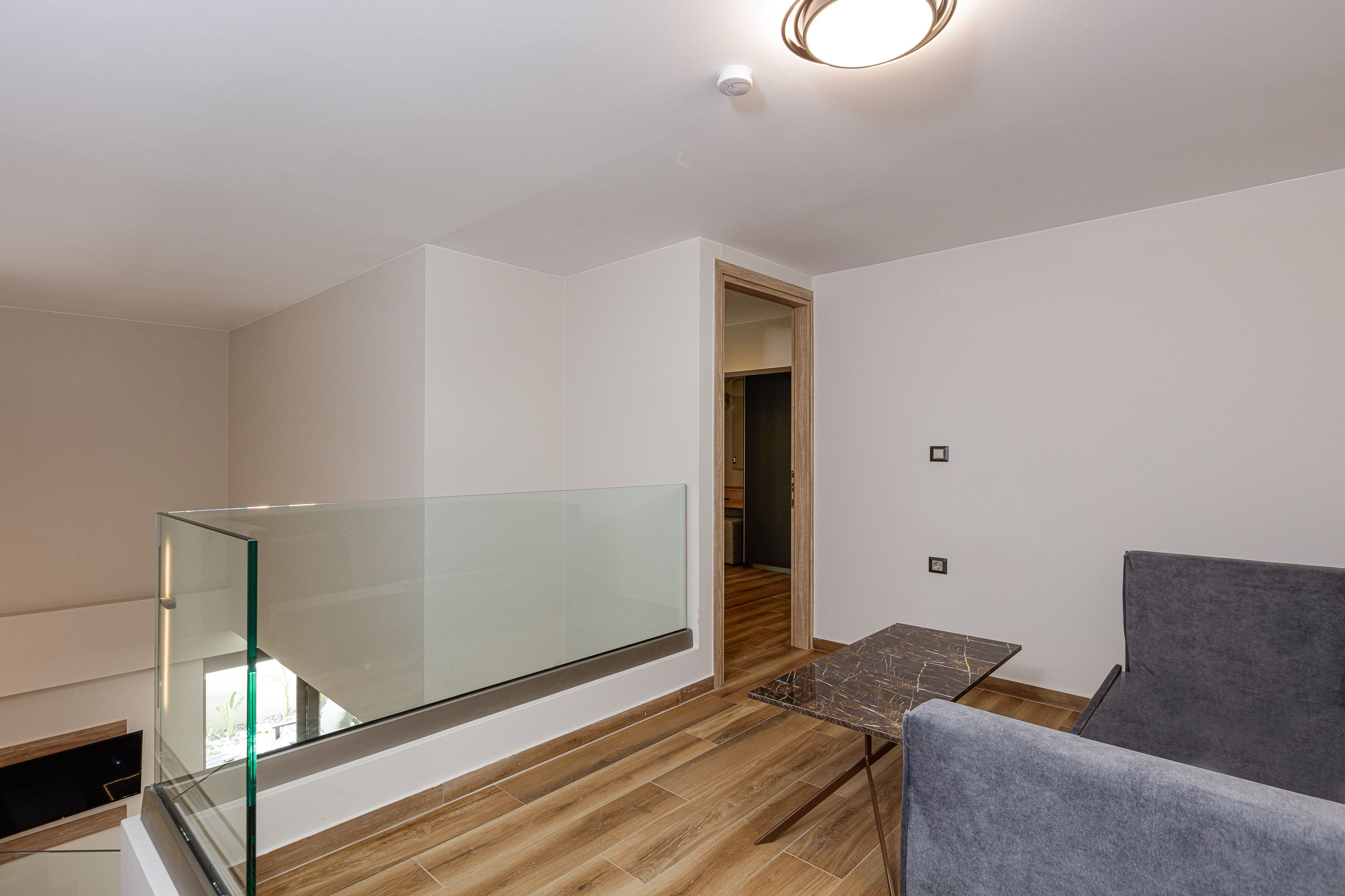 A modern interior with a glass balcony, a dining area with a table and chairs, and a wooden floor.