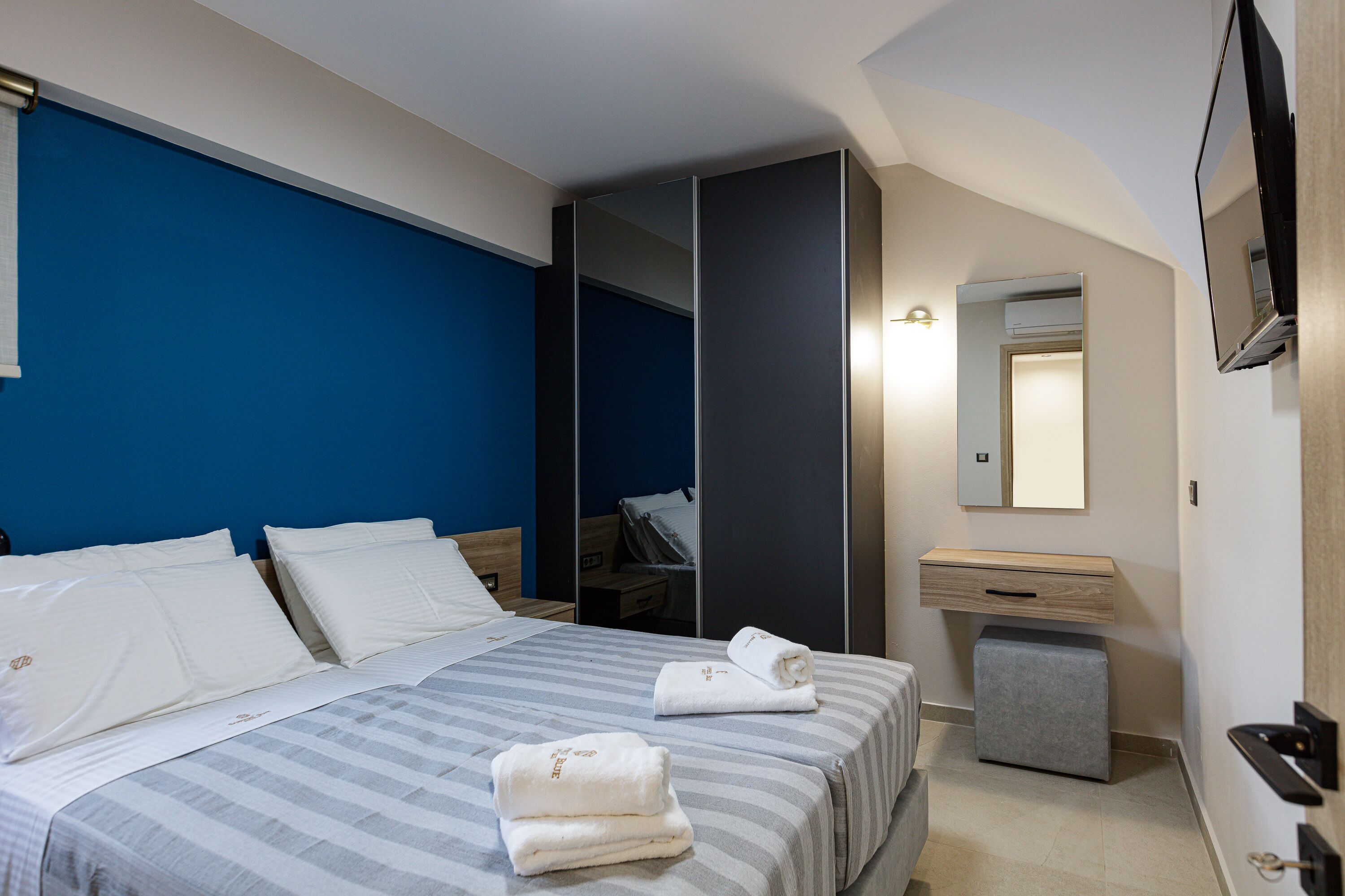 Habitación de hotel con cama, mesita de noche, espejo, armario y un pequeño banco.