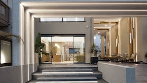 A modern hotel lobby with a staircase leading to the entrance, a seating area with chairs, and a visible kitchen area. - Sapphire Blue Suites (Kissamos)