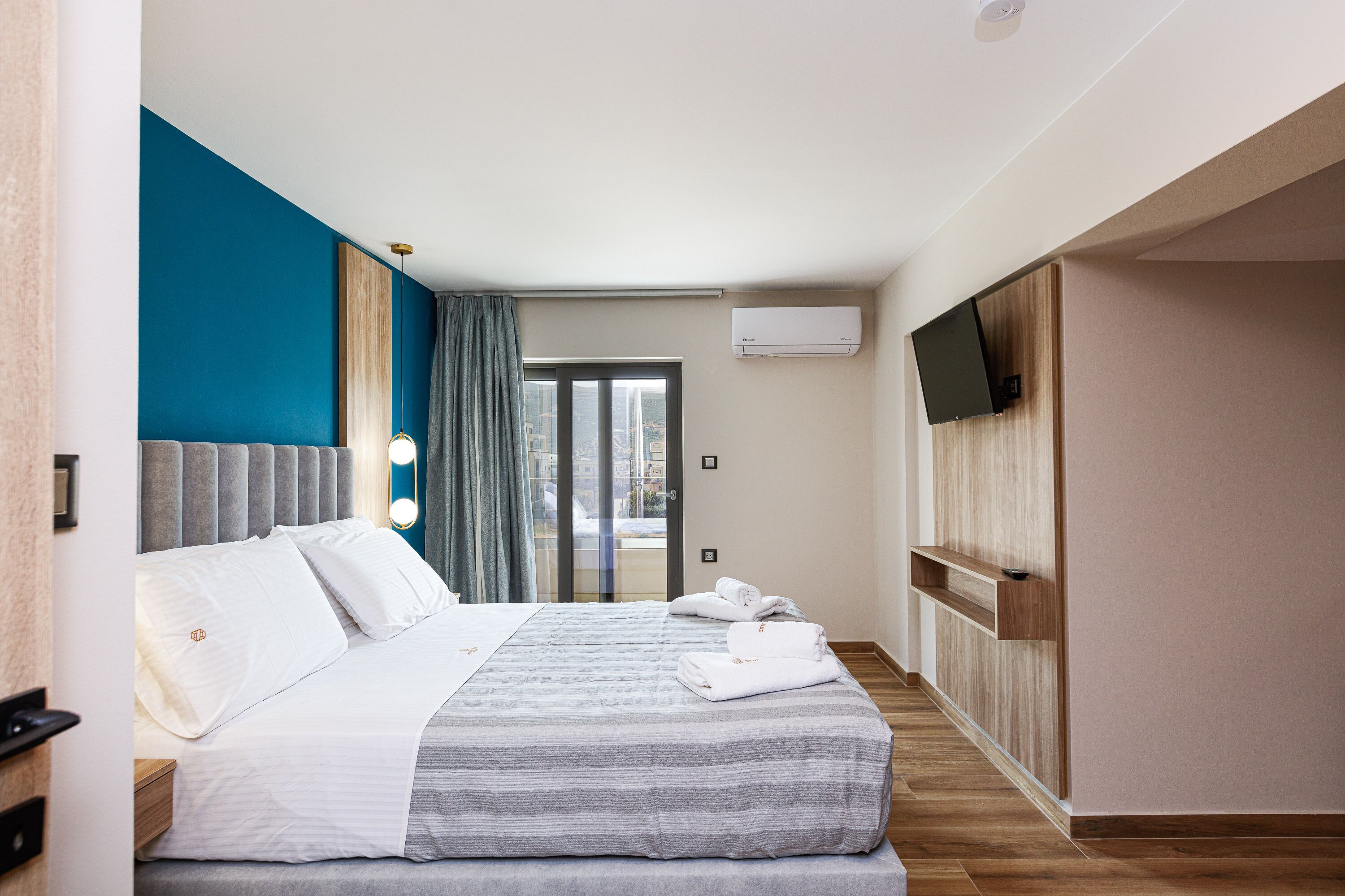 A hotel room with a bed, a TV mounted on the wall, and a window with curtains.