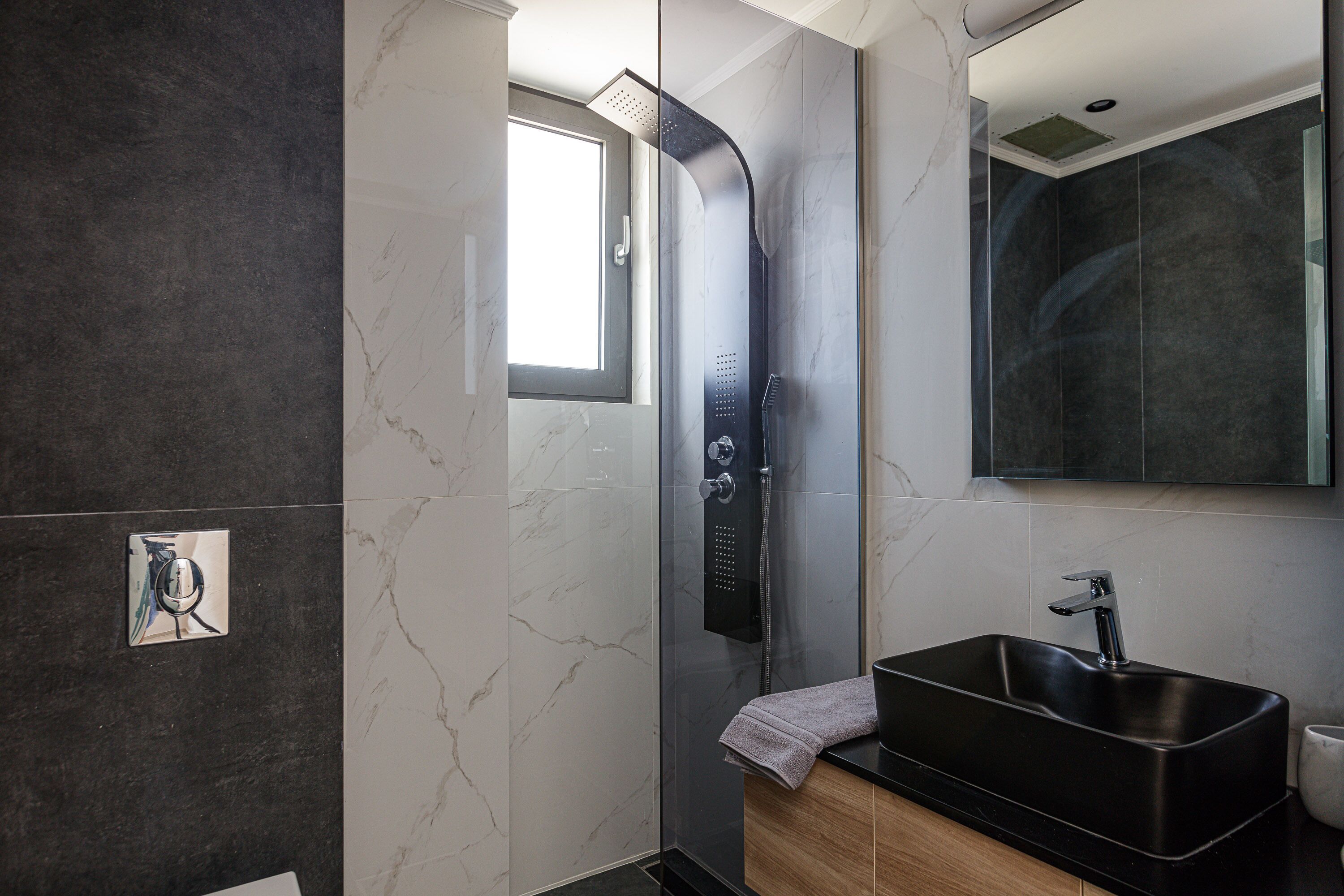 A modern bathroom with a glass-enclosed shower, a black sink, and a marble-tiled wall.