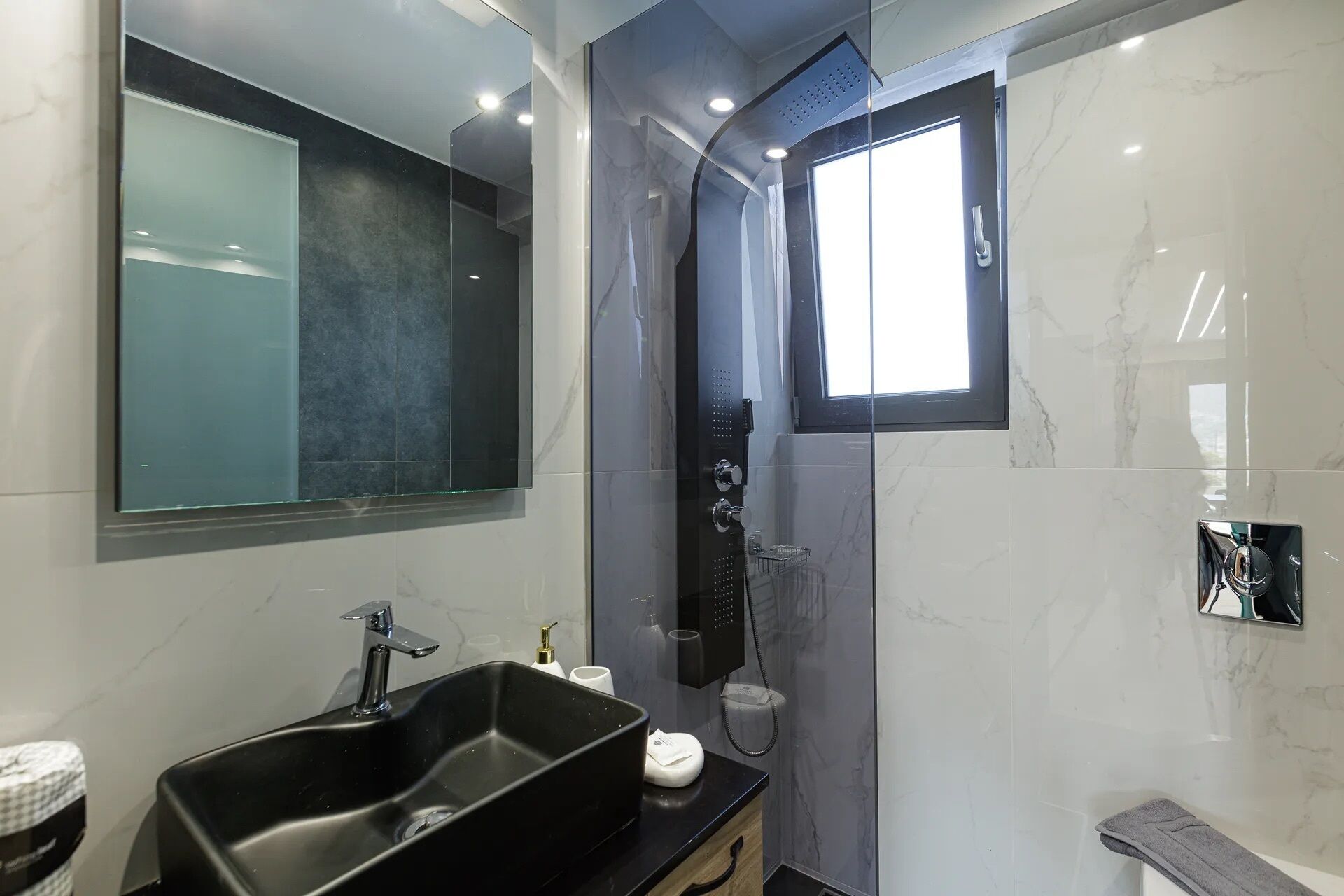Ein modernes Badezimmer mit einem schwarzen Waschbecken, einer Duschkabine aus Glas und einer Wand mit Marmorplatten.