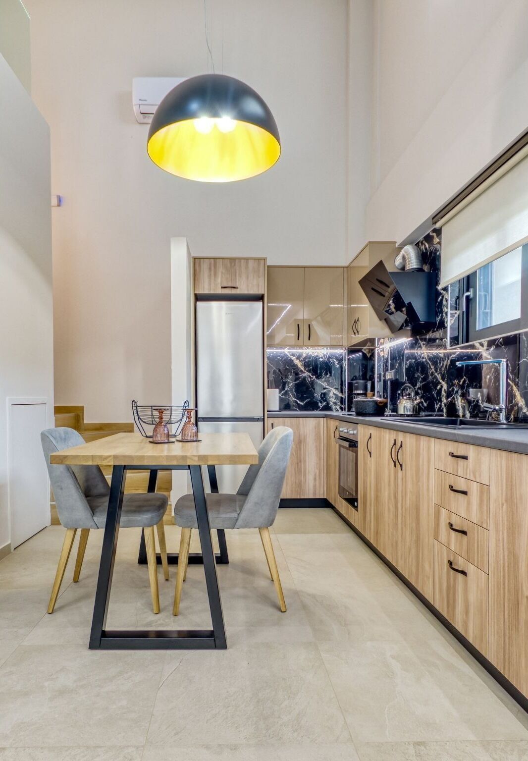 A modern kitchen with a marble countertop, wooden cabinets, and a pendant light.